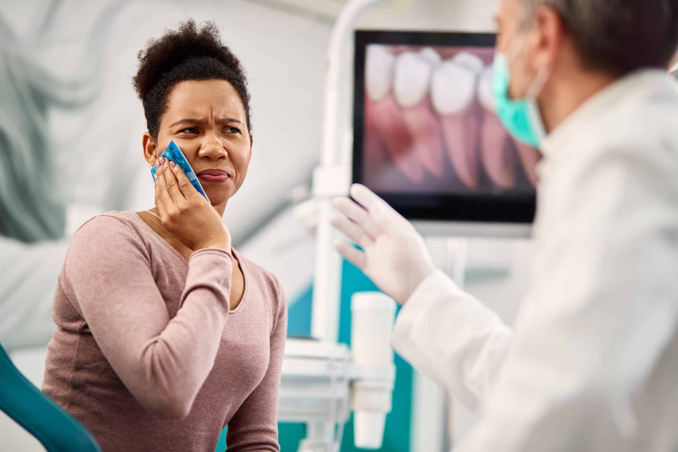Patient holding ice pack on cheek while speaking with emergency dentist about severe tooth pain in clinic