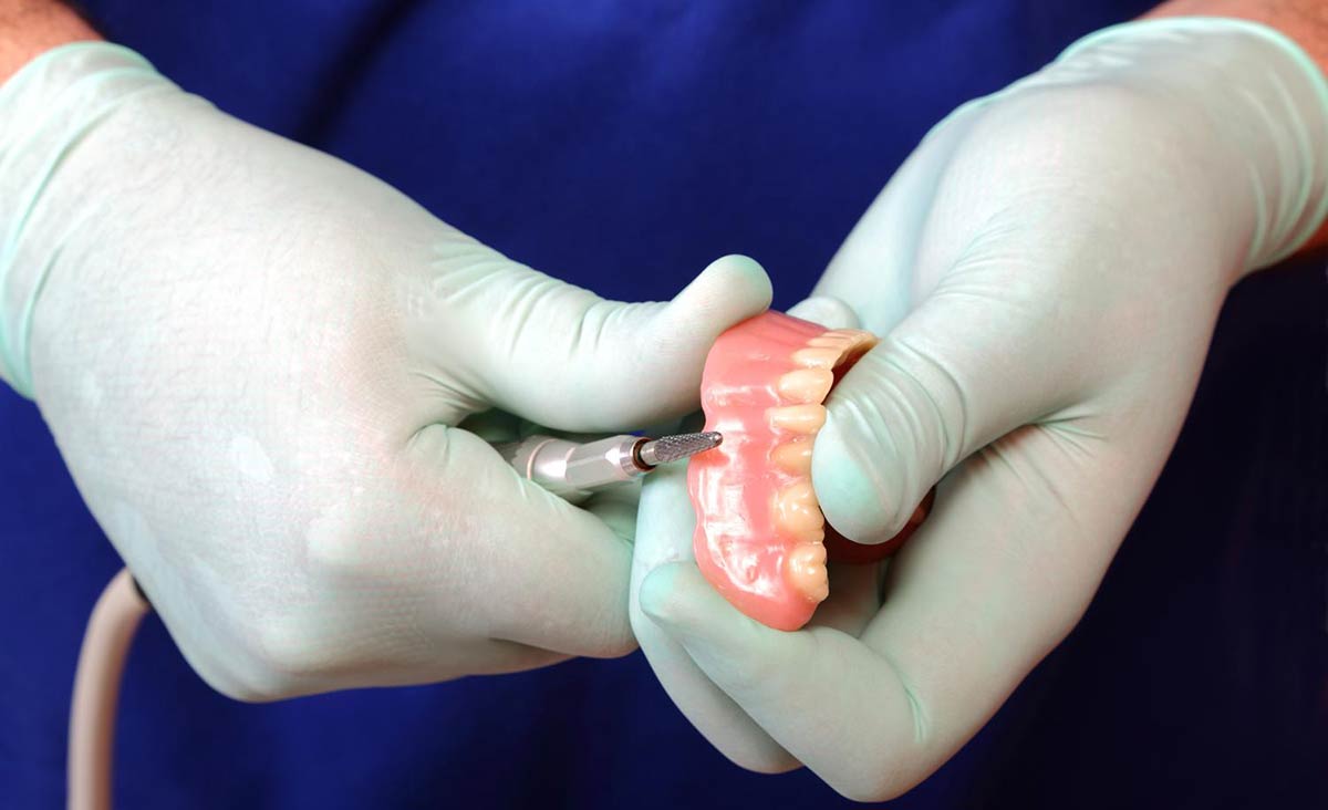 Dental professional adjusting a removable denture with a dental handpiece during a fitting appointment.